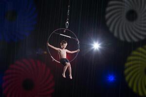 esegue un' circo poco ragazzo artista. circo aereo ginnasta su il cerchio. acrobazie. un' bambino esegue un acrobatico trucco nel il aria foto