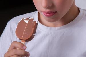 un' ragazzo il cui, di chi viso è irriconoscibile mangia ghiaccio crema coperto nel cioccolato. foto