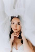 ritratto di il sposa nel il Hotel camera. un' bellissimo giovane ragazza è vestito nel un' bianca nozze vestire. moderno nozze acconciatura. naturale trucco. foto