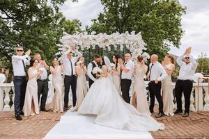 il sposa e sposo e loro amici posa vicino il arco. lungo treno di il vestire. elegante nozze. estate nozze nel natura foto