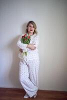ritratto di un' bellissimo di medie dimensioni donna nel pigiama con un' mazzo di rosso tulipani nel un' minimalista stile foto