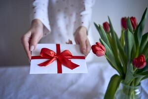 regalo certificato nel rosso e bianca colori nel femmina mani con rosso tulipani foto