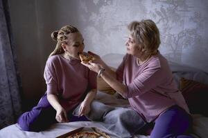 vecchio madre e di mezza età figlia mangiare Pizza e Guardando un' film a casa foto