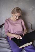 un anziano donna lavori con il computer portatile a casa foto