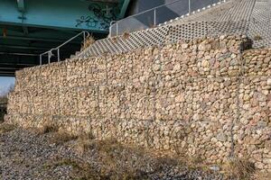 ingegneria struttura fatto di pietre dietro a metallo filo reticolato per rafforzare il fiume banca vicino il strada ponte foto