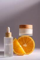 agrume cosmetici con vitamina c e arancia fette su grigio sfondo. viso siero nel contagocce bottiglia e crema barattolo. vuoto confezione per design foto