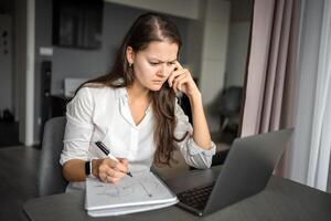 giovane stanco donna utilizzando il computer portatile nel casa posto di lavoro, scrittura Appunti, femmina alunno apprendimento e Guardando in linea seminario web o ascoltando Audio corso, e-learning formazione scolastica concetto. foto