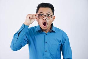 sorpreso o shock bello asiatico uomo con bicchieri nel indossare blu camicia apertura bocca e mano Tenere bicchieri su isolato bianca sfondo foto