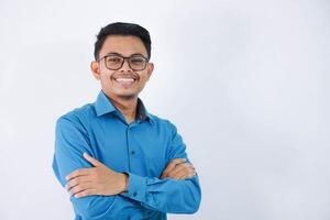 Sorridi o contento asiatico uomo d'affari con bicchieri attraversato braccia e guardare telecamera indossare blu camicia isolato su bianca sfondo foto