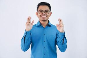 sorridente asiatico uomo d'affari attraversato il suo dita e guardare telecamera indossare blu camicia isolato su bianca sfondo foto