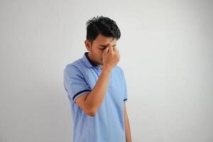 vertigini o depressione ritratto giovane asiatico uomo Tenere naso indossare blu polo t camicia isolato su bianca sfondo foto