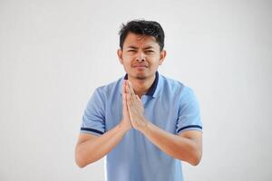 giovane asiatico uomo indossare casuale blu t camicia al di sopra di bianca sfondo accattonaggio con mani insieme con speranza espressione su viso molto emotivo e preoccupato. mendicare. triste viso foto