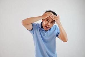 asiatico uomo testa nel dolore, Tenere testa con tutti e due mani indossare blu t camicia isolato su bianca sfondo foto
