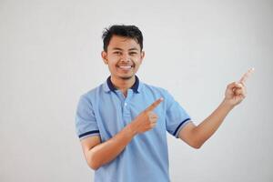 sorridente asiatico uomo con dita puntamento per il lato indossare blu t camicia isolato su bianca sfondo foto