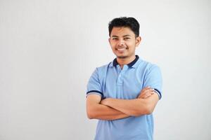 Sorridi o contento asiatico uomo attraversato braccia e guardare telecamera indossare blu t camicia isolato su bianca sfondo foto