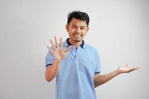 attraente asiatico uomo con mano gesto posa rifiuto o divieto mentre puntamento per copia spazio di il suo lato indossare blu t camicia isolato su bianca sfondo foto