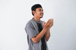 religioso giovane asiatico musulmano uomo con Aperto occhi pregando, Tenere palme viso su, sussurrando pregare, isolato su bianca sfondo. religione Islam, credere concetto foto