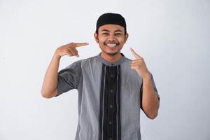 giovane asiatico musulmano uomo indossare koko Abiti sorridente fiducioso mostrando e puntamento con dita denti e bocca. Salute concetto. isolato su bianca sfondo foto