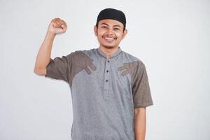 sorridente giovane asiatico musulmano solleva braccia cazzotto e mostrando muscolo indossare koko Abiti isolato su bianca sfondo foto