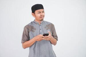 triste viso giovane asiatico musulmano uomo Tenere mobile Telefono mentre ricevuto cattivo notizia indossare musulmano Abiti isolato su bianca sfondo foto