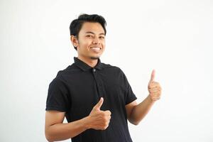 contento o sorridente giovane asiatico uomo dando Due pollici su indossare nero polo t camicia isolato su bianca sfondo foto
