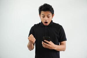 sorpreso o scioccato giovane asiatico uomo isolato su bianca sfondo Tenere Telefono e mani nel pugni con invio un' Messaggio foto