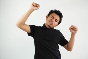 sorridente o contento giovane asiatico uomo stretto il suo pugni applauso spensierato e emozionato. vittoria concetto, indossare nero polo t camicia isolato su bianca sfondo foto