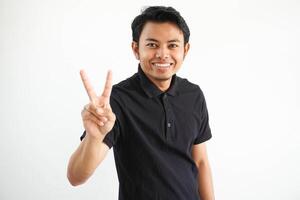 giovane asiatico uomo sorridente contento con tutti e due mano mostrando pace cartello indossare nero polo t camicia isolato su bianca sfondo foto