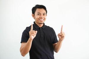 giovane asiatico uomo sorridente contento e puntamento tutti e due mani su indossare nero polo t camicia isolato su bianca sfondo foto