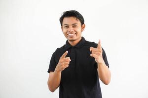 giovane asiatico uomo sorridente e puntamento in direzione telecamera indossare nero polo t camicia isolato su bianca sfondo. foto