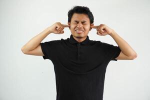 arrabbiato giovane asiatico uomo vicino il suo orecchie con dita indossare nero polo t camicia isolato su bianca sfondo foto