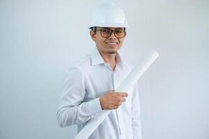 sorridente giovane asiatico architetto indossare casco elmetto protettivo e Tenere progetto carta Piano isolato su bianca sfondo. foto