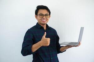 giovane asiatico uomo sorridente fiducioso e dare pollice su mentre Tenere un' il computer portatile computer isolato su bianca sfondo. foto