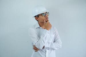 giovane asiatico maschio ingegnere indossare bianca difficile cappello Tenere mento pensiero per costruzione opera isolato su bianca sfondo, copia spazio. foto