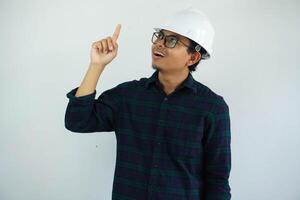 eccitato giovane asiatico architetto uomo indossare bianca difficile cappello sicurezza casco con dito puntamento su isolato su bianca sfondo foto