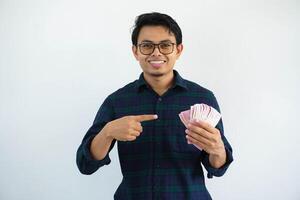 sorridente giovane asiatico uomo mostrando contento espressione mentre puntamento per i soldi quello lui hold isolato su bianca sfondo foto