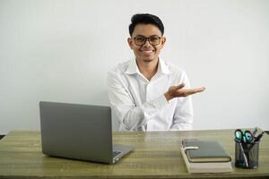 giovane asiatico uomo d'affari nel un' posto di lavoro presentazione un idea mentre guardare sorridente in direzione, indossare bianca camicia con bicchieri isolato foto