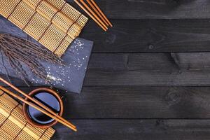 sfondo per Sushi. bambù stuoia e soia salsa su nero di legno tavolo. superiore Visualizza con copia spazio foto