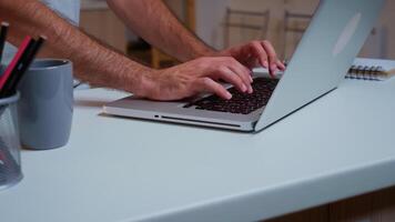 vicino su di dell'uomo mani digitando su il computer portatile seduta nel il cucina in ritardo a notte e Lavorando. occupato dipendente utilizzando moderno tecnologia Rete senza fili fare col tempo per lavoro lettura scrivere, ricerca foto