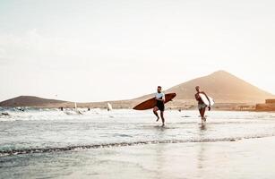 contento surfer coppia in esecuzione con tavole da surf lungo il mare riva - sportivo persone avendo divertimento andando per Surf insieme a tramonto - estremo fare surf sport e gioventù relazione stile di vita concetto foto