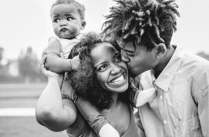 contento africano famiglia avendo divertimento nel un' parco all'aperto - madre e padre con loro figlia godendo tempo insieme nel un' fine settimana giorno - amore e felicità concetto - nero e bianca modificare foto