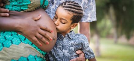 contento africano famiglia aspettandosi altro bambino - vicino su bambino baci pancia di il suo incinta madre - genitori amore e maternità stile di vita concetto foto