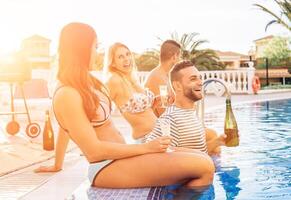 gruppo di contento amici fabbricazione un' piscina festa a tramonto - giovane persone ridendo e avendo divertimento potabile Champagne nel vacanza - amicizia, vacanze, gioventù stile di vita concetto foto