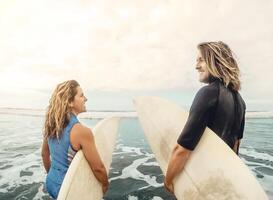 surfers coppia in esecuzione insieme con tavole da surf su oceano a tramonto tempo - sportivo in forma amici avendo divertimento fare surf su alto onde - viaggio e estremo sport cultura stile di vita concetto foto