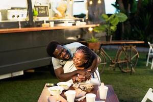 contento afro madre e figlio avendo divertimento mangiare nel un' strada cibo camion mercato all'aperto foto