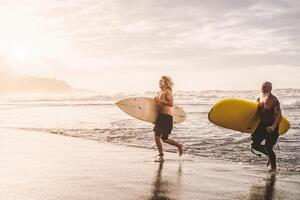 contento in forma amici avendo divertimento fare surf su tramonto tempo - surfers padre e figlio in esecuzione su il oceano - sportivo persone stile di vita e estremo sport concetto foto