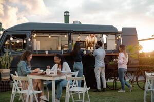 contento multirazziale persone avendo divertimento mangiare nel un' strada cibo camion mercato foto