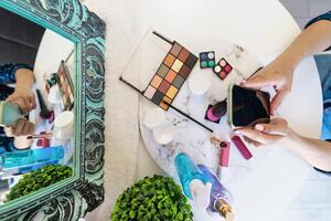 superiore Visualizza giovane donna utilizzando mobile smartphone mentre fare trucco a casa - bellezza cosmetico industria e tecnologia dipendente persone concetto foto