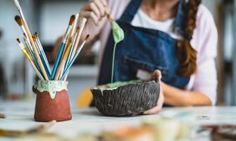 donna miscelazione dipingere con spazzola dentro ceramica ciotola nel laboratorio studio - artigiano opera e creativo mestiere concetto foto