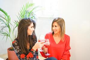 contento donne tostatura e applauso bicchieri di rosso vino nel appartamento - giovane amici avendo divertimento potabile a casa - amicizia, bevande, stile di vita concetto foto